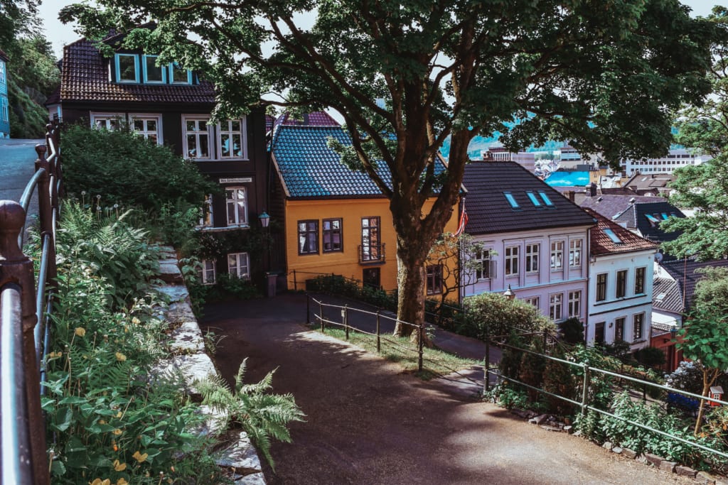 Bergen might be one of the most sought-after cities in Europe for its charm, history, and postcard-perfect setting on the fjord. Here's my guide on how to explore Bergen in 24 hours. PHOTOGRAPHY PROPERTY OF SVADORE As Patrick and I migrated from East to West of Norway in just 4 days, we made it to our final city and the one of the oldest port cities in Europe, Bergen. You can catch more on our journey from Flam to Bergen via a ferry on the stunning Sognefjord in Uncovering the Sognefjord From Flam to Bergen Via Ferry. With 1 day to spare, we decided to see as much as we could of the city. As our ferry pulled into the port 8PM on this sunny May day, we immediately saw the famed colored houses of Bryggen. They reminded me of the houses you would use to play Monopoly all stacked up nicely one next to the other creating a perfect rainbow. Locals and tourists speckled the street in front of the houses, dining in front of them right on the wharf. Bergen is known for its rain. If you think London is rainy, you are wrong. Bergen is considered the rainiest city in the world. It rains 240 days per year! If you want to witness a rare sighting in Bergen, visit the city in late May/early June like Pat and I did. The 2 days we were there we saw nothing but sun (literally both during the night and day due to the sun never truly setting). We dropped our bags off at our Airbnb just a 10 minute walk from the wharf and made our way in search of dinner. More on that in my next post! As soon as we stepped out of our Airbnb we immediately were immersed into Bergen's picture perfect atmosphere. The sun was "setting," as much as it can in Bergen in the summer, creating a pink aura over the cobblestone streets and houses. The next morning as Pat I walked out to grab breakfast and explore the city, we noticed a a graffiti masterpiece a few yards down from our Airbnb. Something you'll notice about Bergen is that although it is famous for it's historical architecture, it is a very alternative city. In fact, it is gaining a new and second reputation as a vivid street art scene. You will see graffiti throughout the city, but not in a vulgar way. Is it a street art that brings satire, recounts history and portrays the artwork of the city. View from our Airbnb balcony The street outside of our Airbnb Without further a due, here's what to see, do and eat in just 24 hours in Bergen: 1. Bryggen We started our journey in UNESCO's Bryggen—or wharf in Norwegian. I like to call this the the postcard motif. It's a mix of bakeries (with amazing pastries!!), hotels, pubs, museums and restaurants. We stopped by one of the bakeries and grabbed some pastries and a cappuccino to get our day started. The pastries at first didn't seem that appetizing to me, but boy oh boy was I wrong. Creamy deliciousness! If there is one thing Norwegian's are good at making—it's pastries!! Finished our breakfast we made our way down the wharf. One thing I love about Norway is how eco-friendly they are about everything, especially water. They try to reuse bottles as much as possible and have stations set up throughout the town were people can refill their water bottles with fresh water so they don't have to waste plastic. Maybe this eco-consciousness is why Norway is such an impeccable country! 2. Øvregaten The street right below our Airbnb and right above Bryggen is Øvregaten. It is considered one of Bergen's main streets and was once the town's main market where cobblers, tailors, artisans and more wood come to trade. Today the road is occupied by antique shops and the occasional tattoo parlor, I mean we are in Bergen after all! 3. Lose Yourself In Bergen's Streets We spent the majority of our morning getting pulled left and right by the adorable streets of Bergen. We originally had a plan, but as we kept walking, every small street was calling our name begging us to explore it. For a look at some of our most favorite streets see below: On our way to grab breakfast 4. Fisketorget Fish Market As it gets closers to lunch time we find ourselves wandering towards the famous Bergen fish market. The market is open every day from the first of May to the end of September. This fish market is again part of the port, fishermen, and trading locations history. It's been an ongoing market since the 1200s and still very much in use today. No need to fear if you come here in the winter, the indoor market located just a few steps from the wharf has the same quality food and is open year round. Fresh caught seafood for sale. Paella with mixed fresh caught seafood offered for lunch. Live caught crabs for sale 5. Skostredet (Art district) Next up, wander around the street of Skostredet, the up and coming street art district in Bergen. Truth be told, you will come across a lot of street are when exploring Bergen, but this area is explicitly dedicated to it not only on it's walls but in it's stores too. 6. Torgallmenningen I recommend you start by walking down Lille Lungegårdsvannet pond and making your way to Marken Street, a quaint cobblestone street with plenty of food options and hidden trinket stores. Then you make your way up to Make your way to Torgallmenningen, or Bergen's Fifth Avenue for an array of activities. Here you can do some shopping, walk by the beautiful Musikkpaviljongen pavillion in Byparken park, sit on the lawn of the newly renovated Art Nouveau theatre, and enjoy lunch at the highly acclaimed Cafe Opera (which is what we did!) Marken Street 7. Klosteret The walk to Klosteret street was one of our favorites. We came across a lot of beautiful old style homes and colorful streets rich in flower pots and immersed in history. Keep walking and you reach the area of Klosteret, Kloster means Monastery in Norwegian. The street is called Klosteret because a famous Monastery used to be here that dates back to 1135. Today it is a beautiful residential area that houses one of our favorite restaurants—Spisekroken! 8. Mount Floyen A trip the top of one of the seven mountains surrounding Bergen, Mount Floyen, is a must when there. We recommend taking the funicular which gets you up there in less than 6 minutes and offers stunning views. An alternate route (and if you have more time) would be to hike up the side of the mountain. That would take roughly 1 hour to get up. From here you can catch breathtaking views of the city, either from the platform balcony they provide or from smaller hidden areas such as the one that Pat and I found below. There is a restaurant at the top where you can enjoy lunch, dinner, snack or a nice cold beer on one of the few sunny days. 9. Tubakuba Many don't know this, but there is more to explore on Mount Floyen than just the view. Roughly 100 yards away from the viewing area hides Tubakuba, a sleekly designed rabbit hole cabin available for anyone to sleep—FREE OF CHARGE. That's right, you heard me. Free. You need to apply to be accepted to sleep in it but you can stay in this quaint rabbit hole with views of the city overlooking Bergen. The only reason Pat and I didn't take it is because we were scared of being so far away from the city, and who knows...bears and coyotes could be roaming this area for all we know. But, if you are not a scaredy cat like me, I would totally jump at the occasion of staying in this architectural masterpiece built by students at the Bergen School of Architecture. A few key things to note before you consider this stay: It does not have electricity, so all heat in the winter is provided by a small wood burning stove and a lot of insulation. I'm not so sure about lights, but I'd assume that isn't something that is available either, you will have to use the light shining through the enormous window in the summer. 10. The Hanseatic Headquarters Bergen is famously known for its history in the Hanseatic League, also called Hansa. It was an organization founded by northern German towns and merchant communities to protect their mutual trading interest. To avoid the crowds of tourist during the day, Pat and I decided to visit in the later afternoon and we recommend you do the same! Since Bergen was one of the first ports in Northern Europe, it seemed fitting to have one of the 4 Hanseatic headquarters set up here. Today, it is the only Hanseatic League headquarters left that is still preserved. Each summer, these German merchants would set up shop in Bergen in the area that we today call Bryggen. It is made up of the wharf and the Hanseatic Headquarters where they once lived. Today it is considered a UNESCO World Heritage Site. In my opinion, the headquarters look identical to Diagon Alley and could have in fact inspired J.K. Rowling. Take a look for yourselves if you don't believe me: The wooden houses that adorn these maze-like and Harry Potter-like streets have caught fire time and time again. The great fire of 1702 turned Bergen to ashes, but rather than rebuild from scratch, the locals kept the original foundation from the 12th century and have rebuilt upon using the old patterns and methods. This is what makes Bryggen such a world marvel! The last fire was in 1955. Because of this effort, today approximately 62 buildings within the Hanseatic Headquarters still remain of this former townscape. The headquarters is set up like it once was with the merchants shops on the ground floor and the merchants homes on the top. As you walk around, you really get a sense of what it was once like back in the day! Pat kissing a moose! 11. Bergunhaus Fortress Welcome to one of the oldest and best preserved fortress' in Norway. It used to house the royal family back in the 13th century. It was a very important fortress back in the day and was even where the first set of laws were drawn up for Norway. Located right at the end of the Bryggen wharf, this fortress is open to the public. We visited later on in the day and unfortunately were not able to see the hall inside. Haakon's hall looks identical to the Great Hall in Harry Potter in my opinion! Another coincidence..? I think not, but that's just my opinion. Google it and let me know if you don't agree. Today the hall is still used for royal dinners and other important events. 12. Happy Hour at Rock & Roll American Diner Now I know what you are thinking. Ugh, typical American stopping by an American diner when abroad instead of immersing herself in the culture. I promise you this is NOT the case with Rock & Roll American Diner. The place is a hot spot in Bergen and filled with locals. They've done a better job at bringing back to life our diners then we have! Imagine eating in an actual car inside the diner (I kid you not, one room is dedicated just to that!), sipping huge milkshakes, a room full of old school jukeboxes and records still playing, vintage tall boys and seats. It's a dream come true and made me feel like I was whisked away back to the 80s. Pat and I stopped here for a quick drink among the locals before heading out to dinner. 13. Dinner at Spisekroken Our night ended with dinner back near Klosteret at Spisekroken. The setting is small and quaint and you wouldn't expect anything to grandiose, but the meal is fit for a Michelin star. Their french-inspired cuisine was out of this world and has Patrick and I still talking about their food to this day. The best duck I have ever had and the best lamb Pat has ever had. More on our dinner in my upcoming posts. Duck from Holte farme served with wild garlic potato carrot pure, baked salsify baked in lemon, honey and wild garlic sauce Gourmet veal from Sogn with parsly and parsley root pure, gooseberry sauce small potatoes, pickled red onions, baked carrot, asparagus and grilled sweet bread. Now I know what you are thinking. Sveva...how on earth did you get that all done in ONE day? I promise you it is possible. The city is small, and you will get distracted continuously by the adorable streets. But if you are out the door by 9AM and out till 10PM, you will manage. As mentioned, the sun never sets in the summer so you have THAT much more time during the day to explore the city and you don't get tired because you're body doesn't understand that it needs to go in night time mode. Bergen is a jewel, no wonder it inspired the setting of Disney's Frozen and in my opinion Harry Potter as well! To uncover its magic and its surrounding nature escapes you definitely will want a few days in the area. But if you are limited in time, follow this guide for a sure fire way to immerse yourself in as much of the city as you can in one day. Get insider travel tips and lifestyle content on the world’s most exceptional destinations, experiences and products directly to your inbox. Don’t miss out–sign up for travel blog SVADORE on the right hand side to stay up-to-date on where to go, what to do, what to see, where to stay, and where to eat around the globe. Follow Svadore on Instagram: @SVADOREand @SVADORE_eats Follow Svadore on Twitter: @SvadoreTravels Follow Svadore on Pinterest: SVADORE Follow Svadore on Facebook: SVADORE